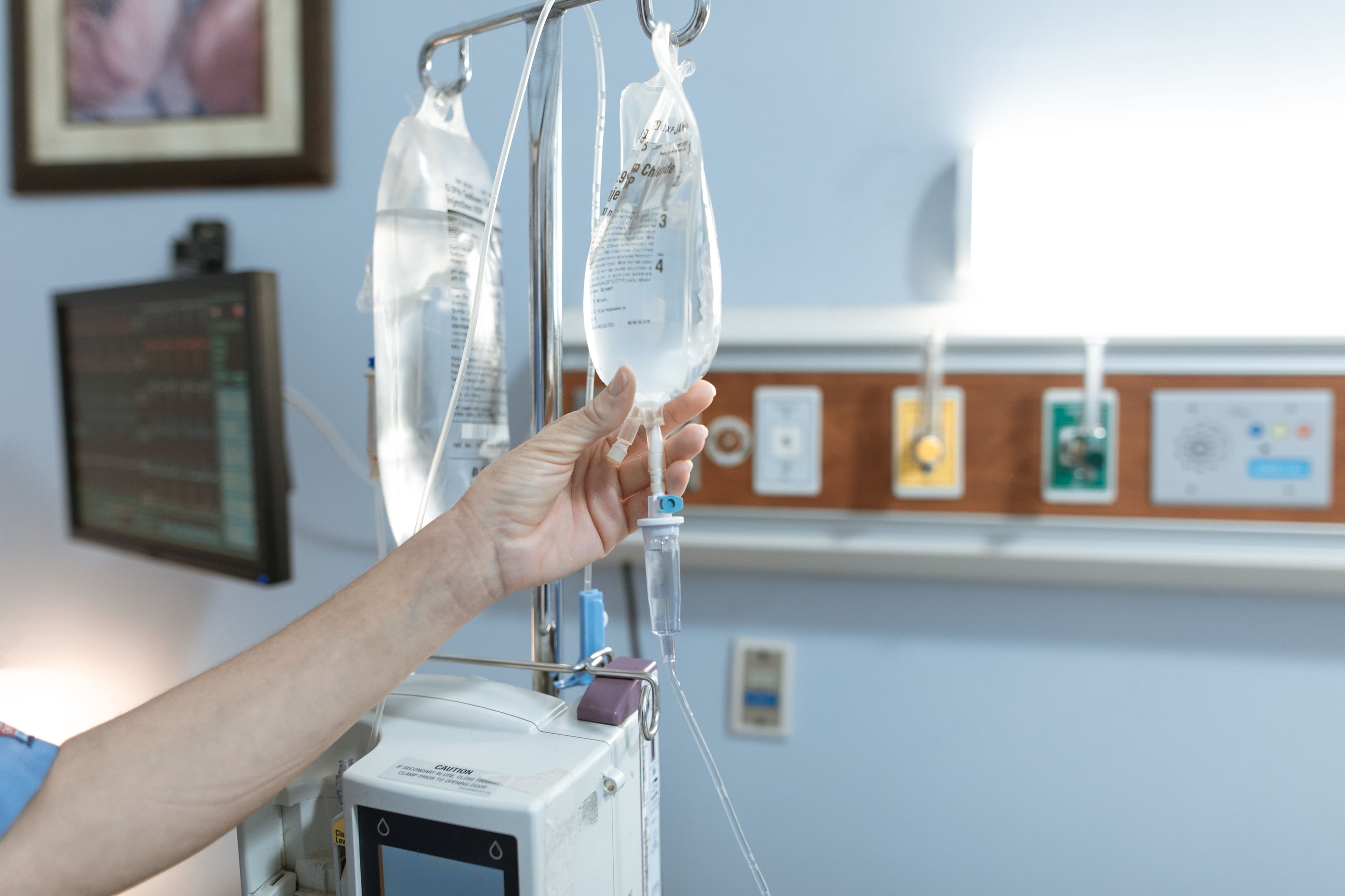 Mão de profissional de enfermagem ajustando soro em paciente durante atendimento hospitalar