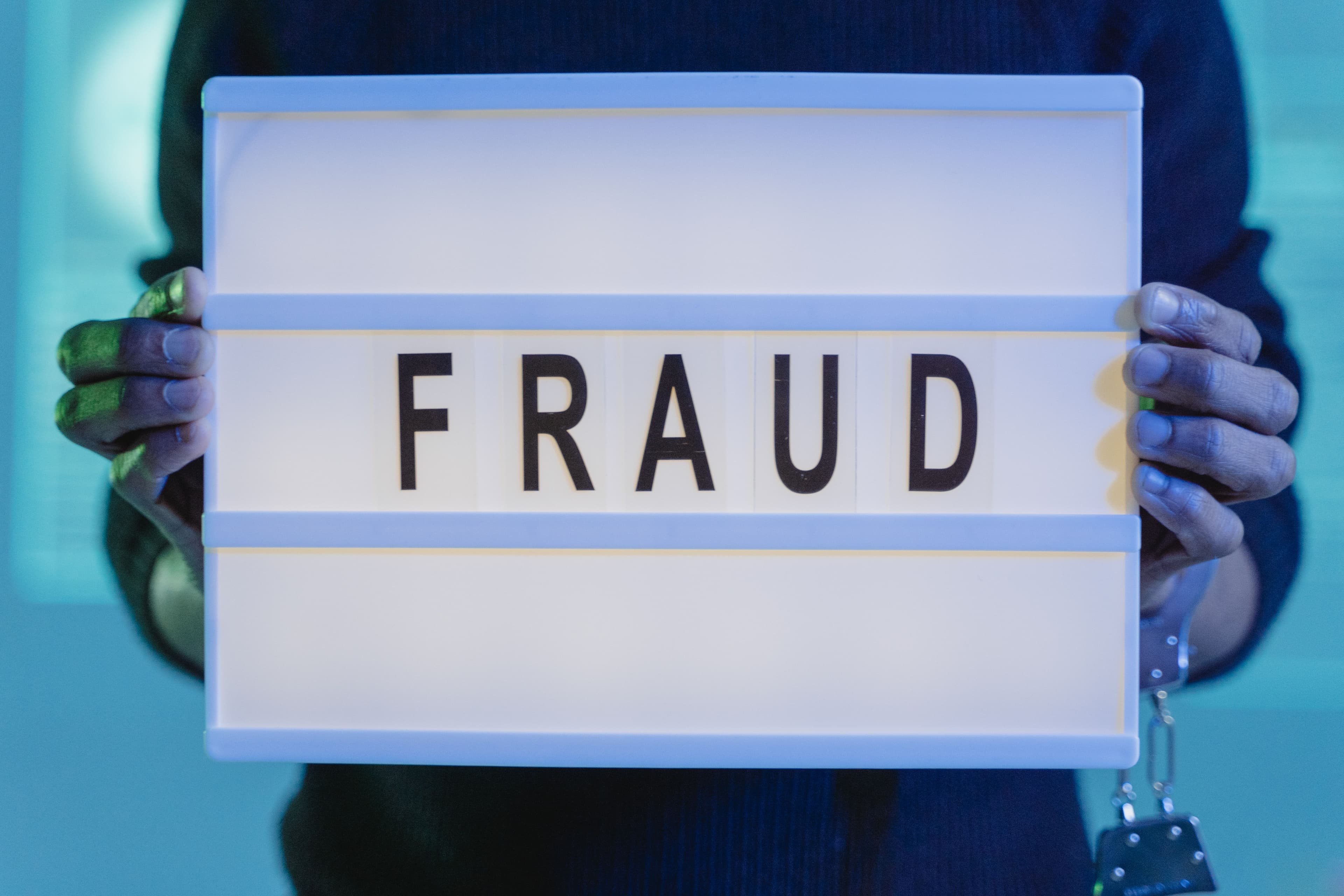 Mãos segurando cartaz com a palavra FRAUD iluminado em azul