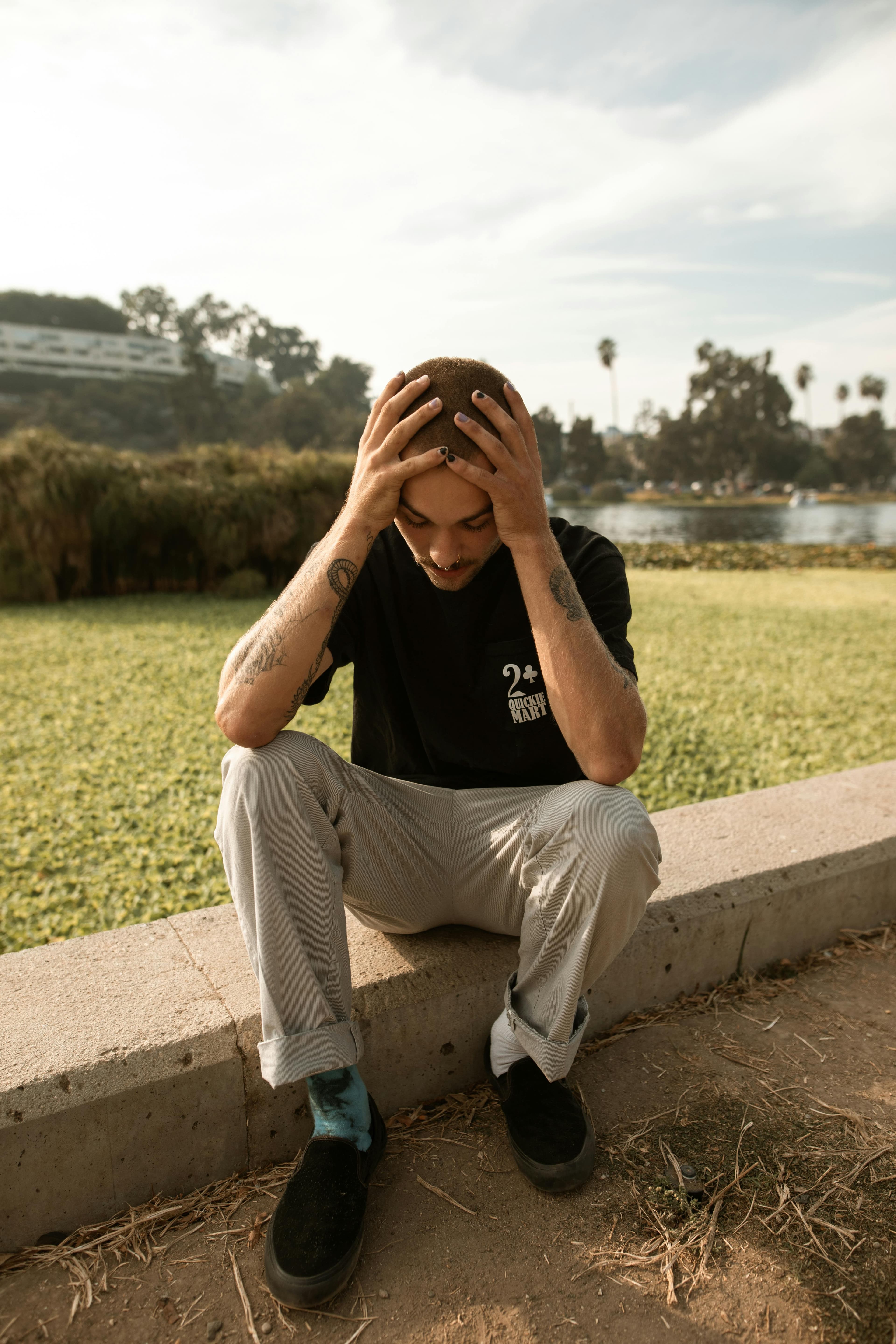 Homem com a cabeça entre as mãos sentado ao ar livre, representando sofrimento emocional